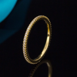 Macro shot of gold-plated eternity ring with pave-set zircon stones on a reflective surface