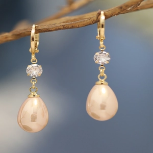 Detailed close-up of gold drop earrings with champagne resin pearls on a branch