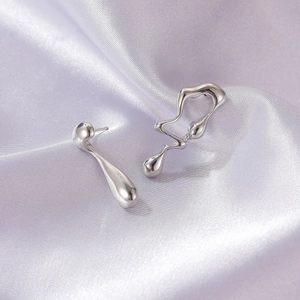 Detailed view of silver asymmetric liquid metal earrings on a purple silk background