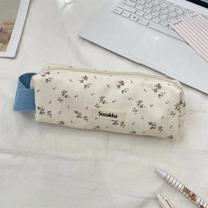 Detail of floral canvas pencil case with blue handle and side brand label on desk