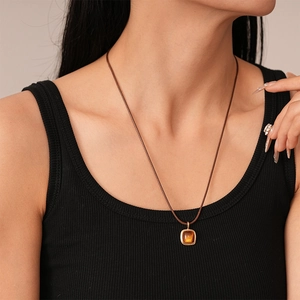 Close-up of a minimalist amber resin square pendant with a gold metal frame on a brown cord