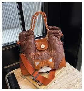 Detail of quilted brown tote bag with plush cat decor and orange woven handle strap