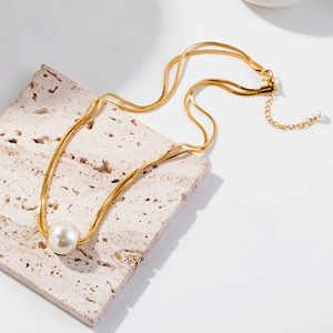 Close-up of double-layered gold snake chain necklace with white pearl on beige stone