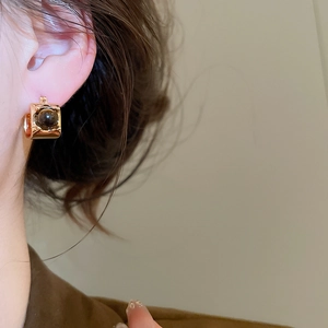 Close-up of gold-plated tiger eye stone earrings worn by a model in warm lighting