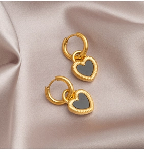 Detail of heart-shaped earrings with black inlay and golden textured metal on silk