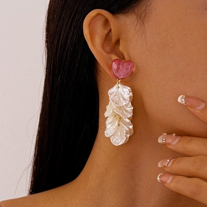 Détail des boucles d'oreilles cœur rose avec pétales en résine blanche sur mannequin femme