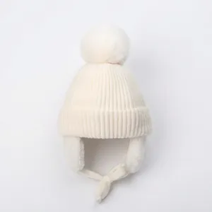 Detail of white winter knit hat featuring a fluffy pom-pom and protective earflaps
