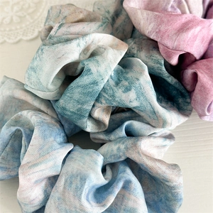 Detailed close-up of blue and pink tie-dye satin scrunchies with soft silk texture