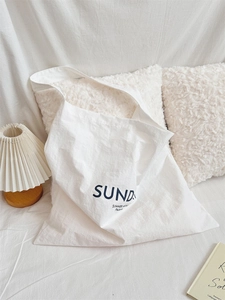 Detail of white canvas tote bag with black minimalist typography in cozy home setting