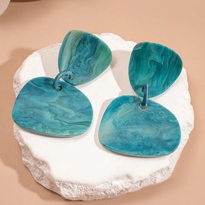 Detail of teal marble resin drop earrings placed on a white stone decorative element