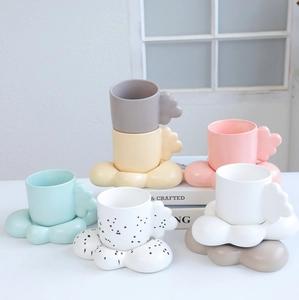Detail of cloud-shaped handles on matte ceramic mugs with matching saucers in pastel colors