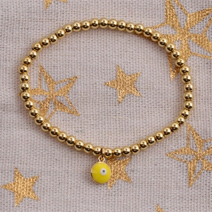 Detailed shot of golden beaded bracelet featuring a yellow enamel evil eye charm on fabric