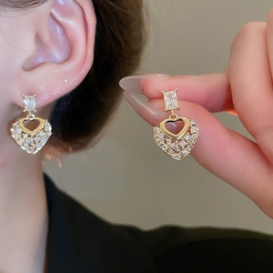 Macro detail of gold-toned heart drop earrings with shimmering zircon pavé stones