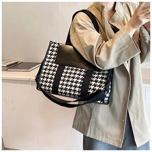 Side view of houndstooth tote bag with black leather trim and wide shoulder strap
