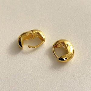 Close-up of minimalist golden oval earrings on a textured off-white background
