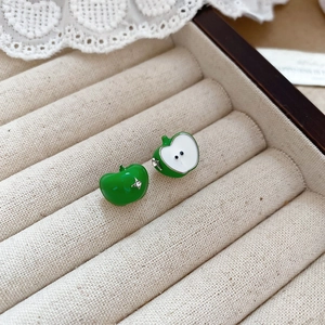Detail of green apple-shaped stud earrings on beige velvet jewelry box with lace