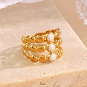 Three-layer gold beaded stainless steel ring with white enamel circles on stone surface