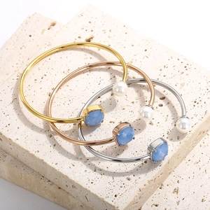 Dettaglio di tre bracciali a C con pietre blu e perle su pietra naturale bianca