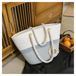 Detail of woven tote bag featuring white and grey panels with daisy flower and rope handle