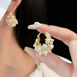 Dettaglio macro di orecchini vintage a C placcati in oro con grappoli di perle bianche
