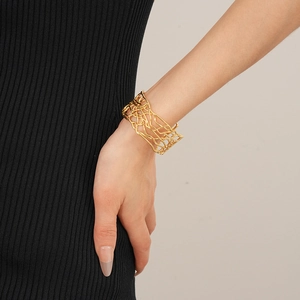 Gros plan d'un bracelet manchette doré évidé porté sur une manche en maille noire
