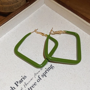 Macro shot of green enamel square hoop earrings inside an elegant beige gift box