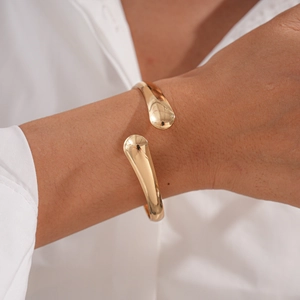 Detail of a polished gold irregular open cuff bracelet featuring smooth teardrop ends
