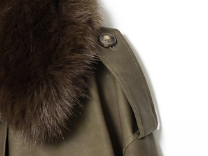 Détail d'un manteau vert armée avec col en fausse fourrure douce et bouton ambre poli