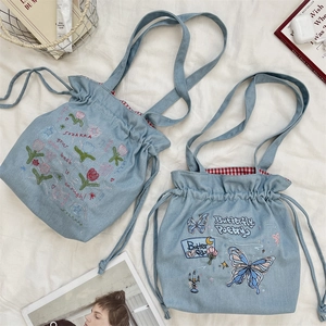 Detail of denim drawstring tote bag featuring floral embroidery and red checkered lining