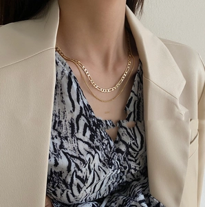 Close-up of layered gold necklaces with figaro and bead chains on model's neck