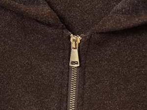 Close-up of a golden metal zipper on a thick dark brown wool fabric hooded jacket