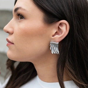 Close-up of a silver irregular fan-shaped pleated earring worn on a model's ear