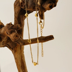 Vue détaillée du collier coeur en acier inoxydable doré suspendu sur un bois naturel