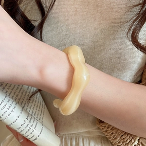 Detail of a wavy beige acrylic bangle on a model's wrist with French aesthetic props