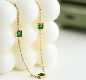 Detailed macro view of gold beaded chain necklace with square emerald green stones