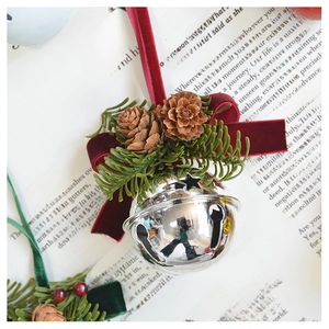 Close-up of a silver Christmas bell with red velvet bow, pine cones, and green pine needles
