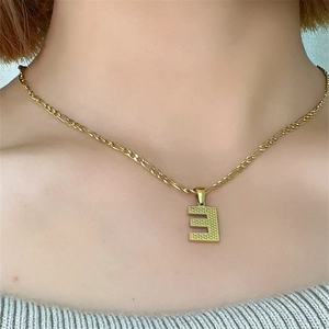 Dettaglio della collana dorata con ciondolo lettera E indossata da una modella