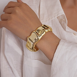 Close-up of a wide gold metal cuff bracelet with irregular wavy texture on a female wrist