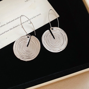 Detail of silver drop earrings with spiral texture resting on a black velvet display