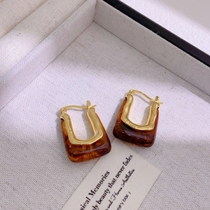 Detail of U-shaped gold-plated earrings with tortoise shell resin inlay on cream velvet