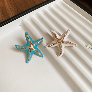 Detail of blue and white enamel starfish earrings on a white velvet display tray