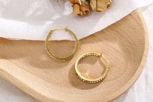 Macro detail of gold 18K plated hoop earrings with micro-paved diamonds on wood