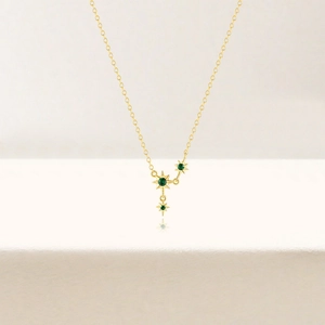 Detail of S925 silver gold star necklace with green crystals on smooth white surface