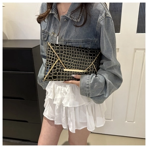 Close-up of woman holding black and gold geometric pattern clutch bag in casual style