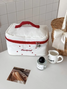 Détail de la trousse à maquillage blanche avec broderie cœur, anse rouge et zip en cœur