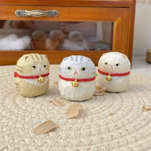 Close-up of three handcrafted miniature wooden cat figurines with gold bells on woven mat