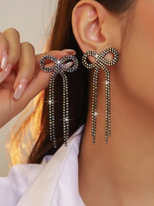 Close-up of model wearing sparkling rhinestone bow earrings with long tassel detail