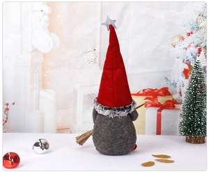 Standing Christmas gnome in red hat with small broom in front of cozy fireplace