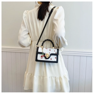 Detail view of the white cherry print crossbody bag with woven handle and cherry charm