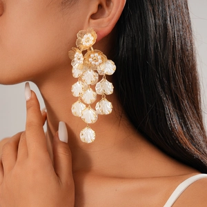 Detail of elegant gold flower drop earrings with white shell tassel worn by a model